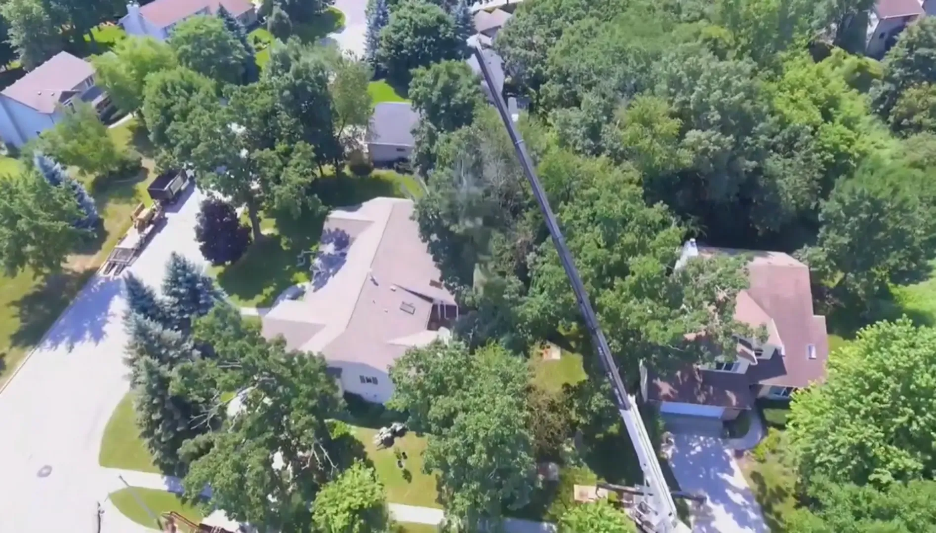 Crane tree removal in Rome, GA — aerial view of a crane boom reaching over a house roof during a tree removal job